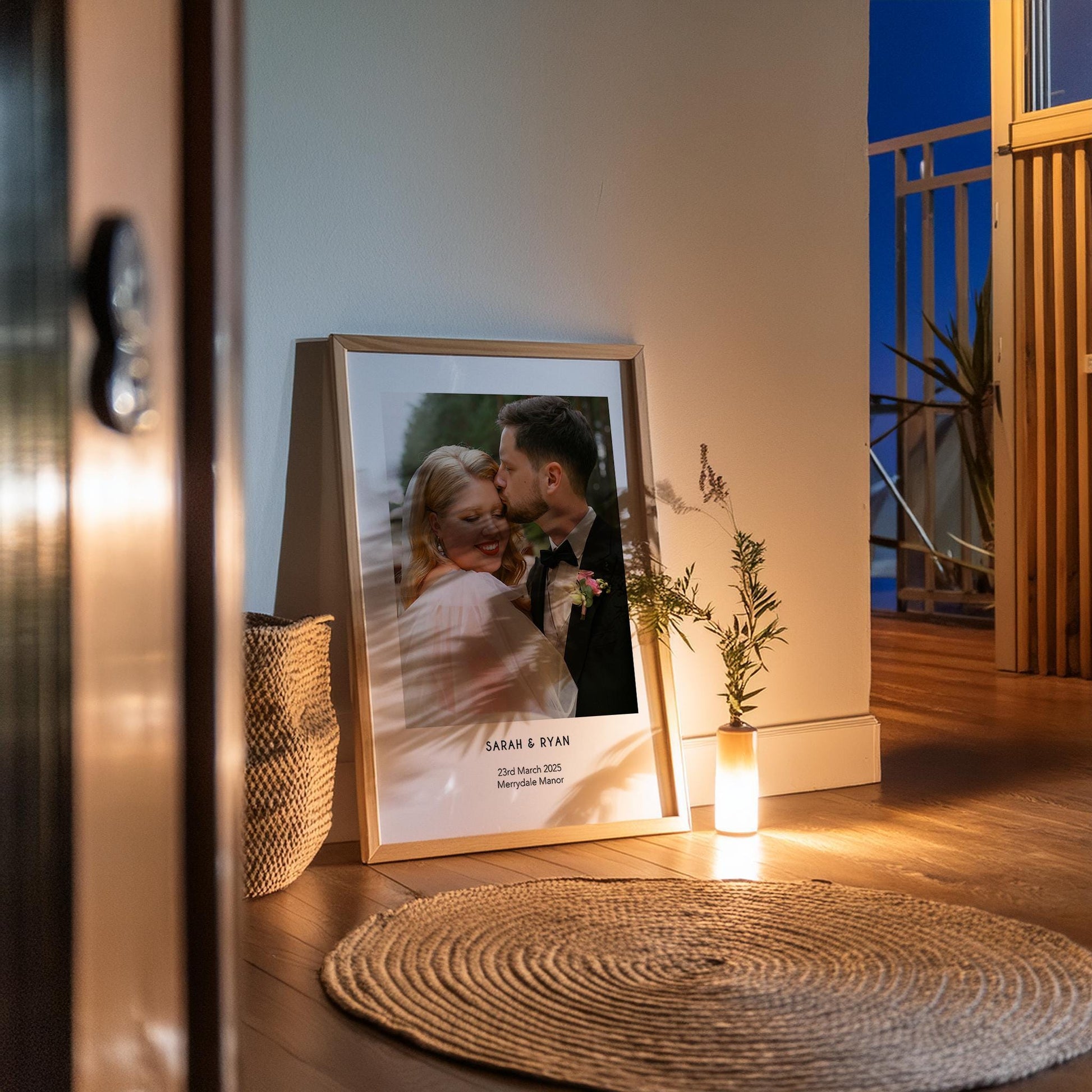 A personalised wedding photo print featuring a couple on their wedding day in elegant natural light. The bride wears an off-shoulder white gown and holds a soft green and white bouquet while the groom embraces her. Minimal modern layout with names, wedding date and venue below the image. A stylish custom keepsake for couples, weddings, anniversaries or home decor.